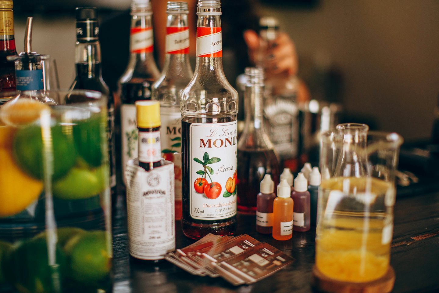 Glass syrup bottles and fruit garnishes on a wooden counter.