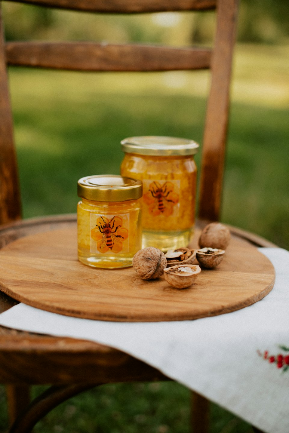 Honey jars and walnuts sit on a wooden board.